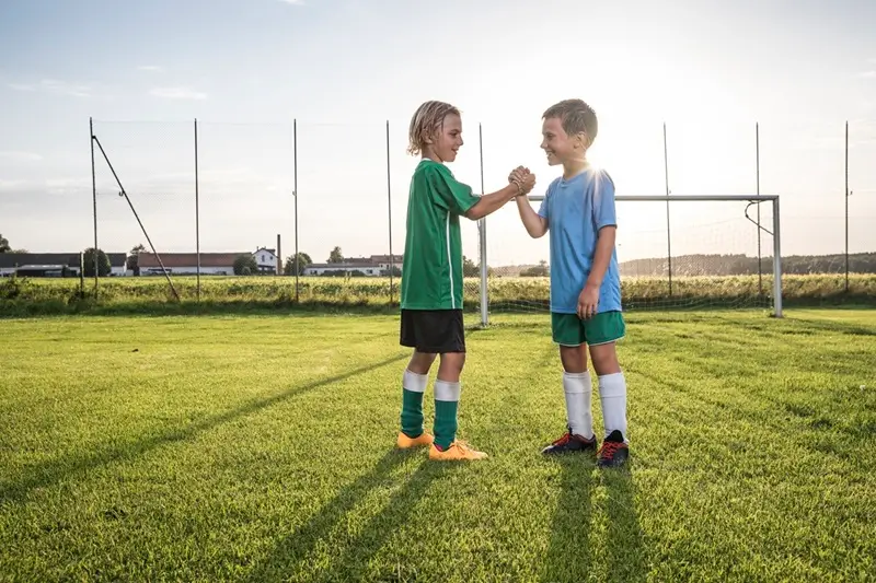 Jovens jogadores canhotos de futebol sorridentes apertando as mãos no campo de futebol