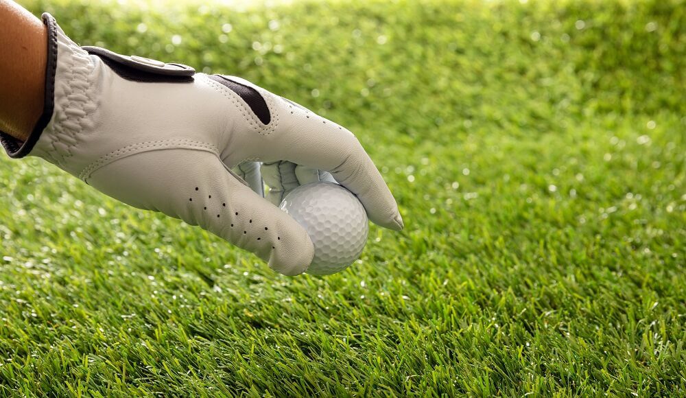 Mão canhota na luva de golfe segurando uma bola de golfe